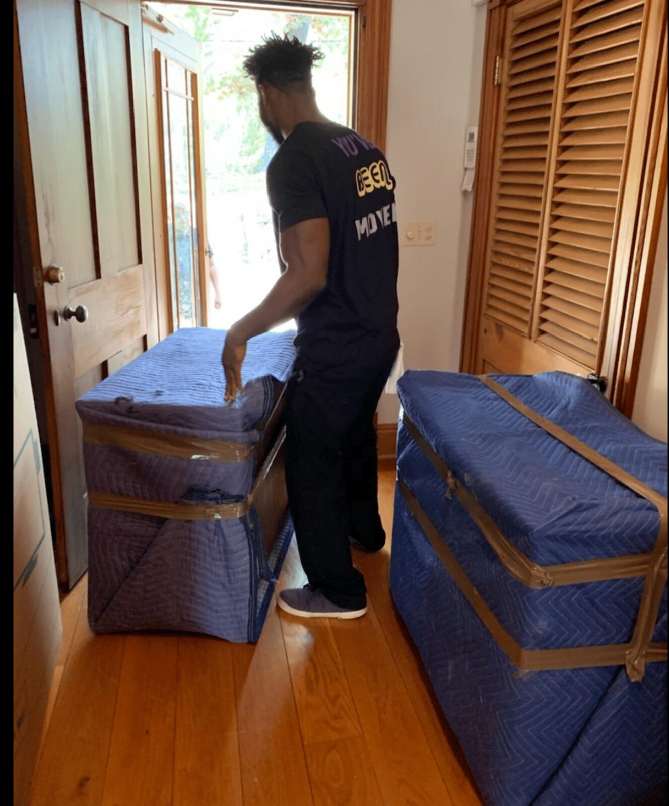 Royalty Moving crew member carrying wrapped furniture to a customer's door